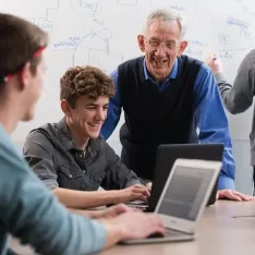 A professor helping students at a computer in a classroom.